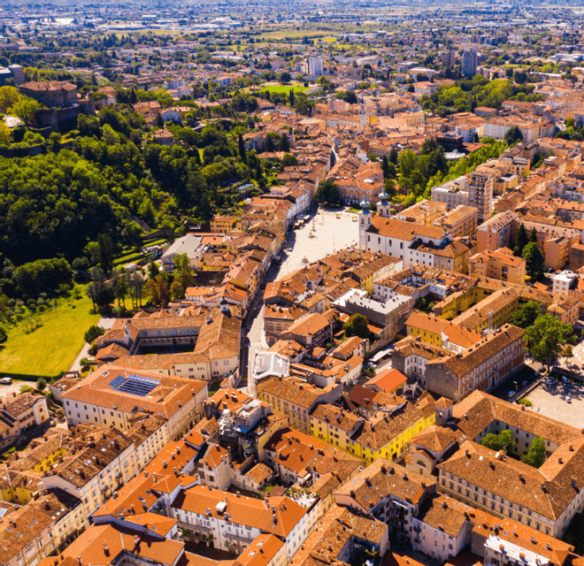 Veduta aerea di una città europea con tetti in terracotta, una piazza centrale e alberi verdi circostanti.