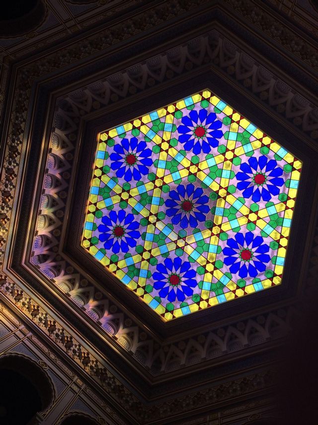 Una vidriera hexagonal en el techo, con un diseño floral geométrico y colorido en tonos azules, verdes y amarillos.