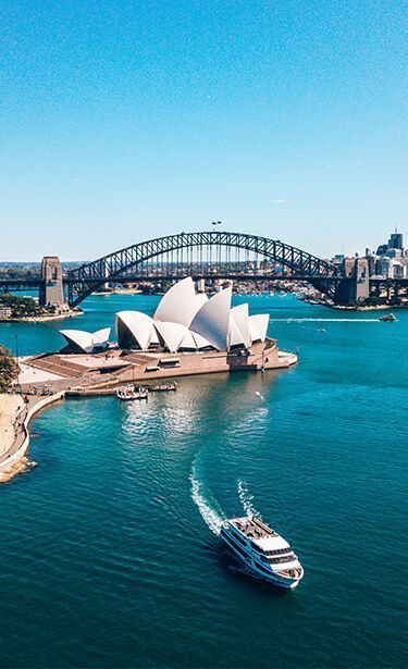 An aerial view of the Sydney Opera House and Harbour Bridge, with a ferry sailing on the bright blue water below.