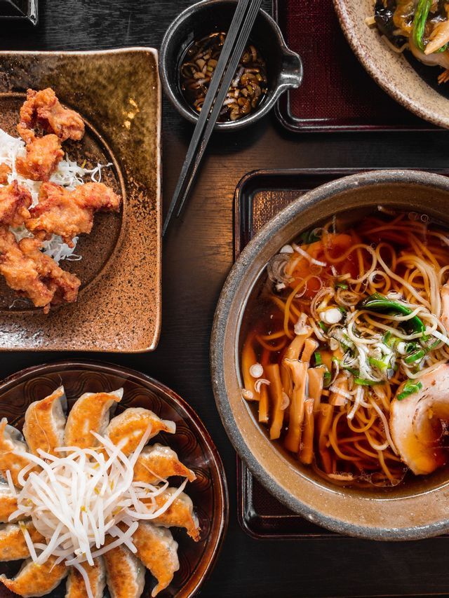 Una vista dall'alto di un pasto giapponese con una ciotola di ramen, un piatto di karaage e ravioli gyoza su un tavolo scuro.