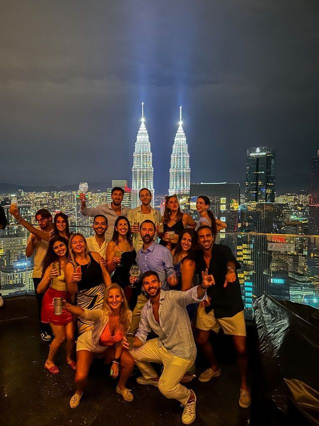 Un gruppo WeRoad posa per una foto su un tetto di notte, con torri gemelle illuminate sullo sfondo.