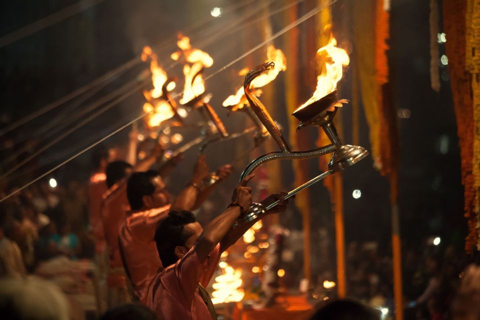 Una fila de hombres con túnicas naranjas realiza una ceremonia espiritual de noche, sosteniendo grandes lámparas llameantes.
