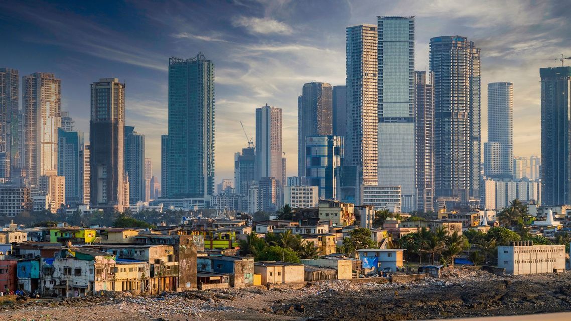 Un paisaje urbano que muestra el contraste entre chabolas en primer plano y rascacielos modernos al fondo.
