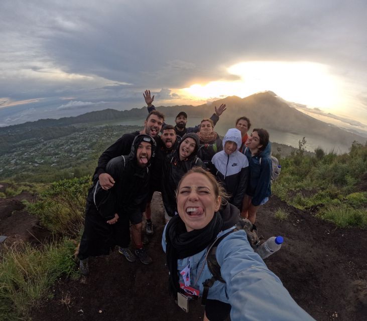 Eine WeRoad-Gruppenreise macht bei Sonnenaufgang ein verspieltes Fisheye-Selfie auf einem Berggipfel mit Blick auf einen Vulkan und einen See.