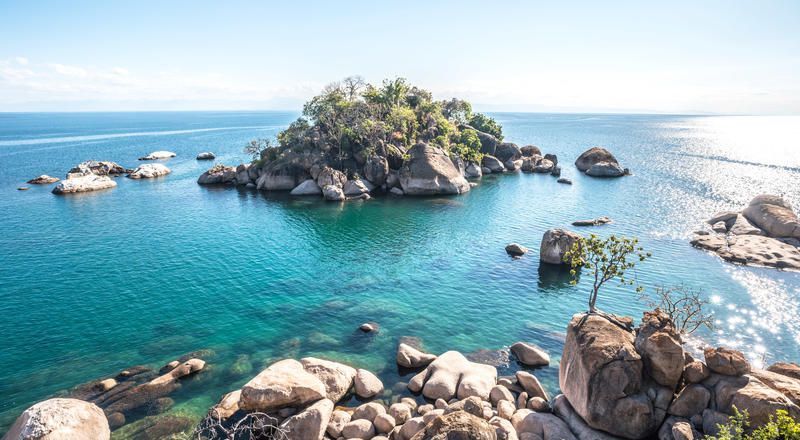 Una piccola isola rocciosa coperta di alberi si trova in acque limpide e turchesi circondata da massi.