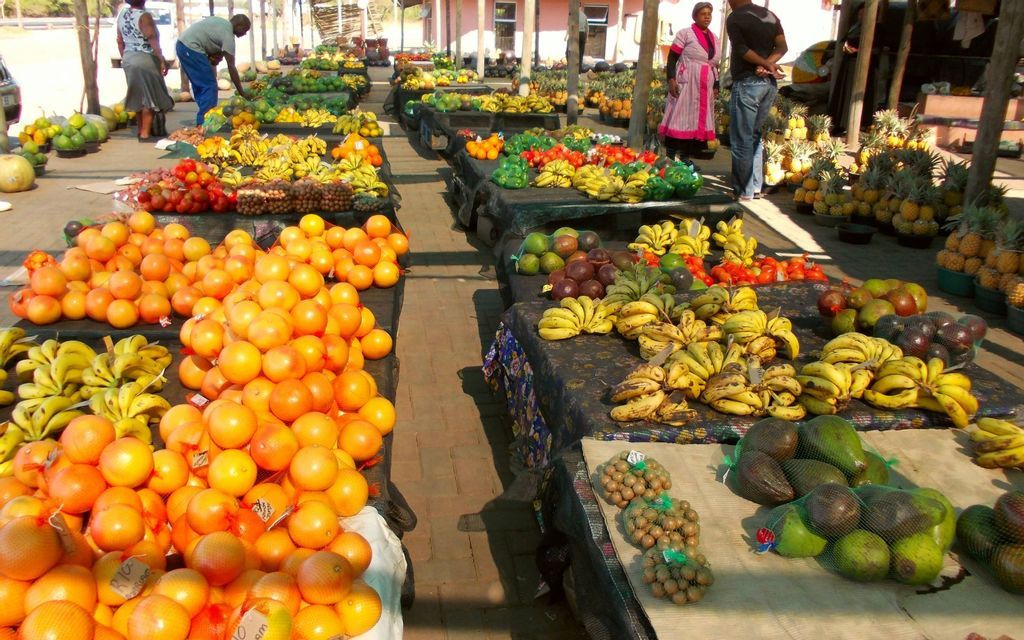 Un mercato all'aperto con lunghe bancarelle che espongono cumuli di arance fresche, banane, avocado e altri frutti tropicali.