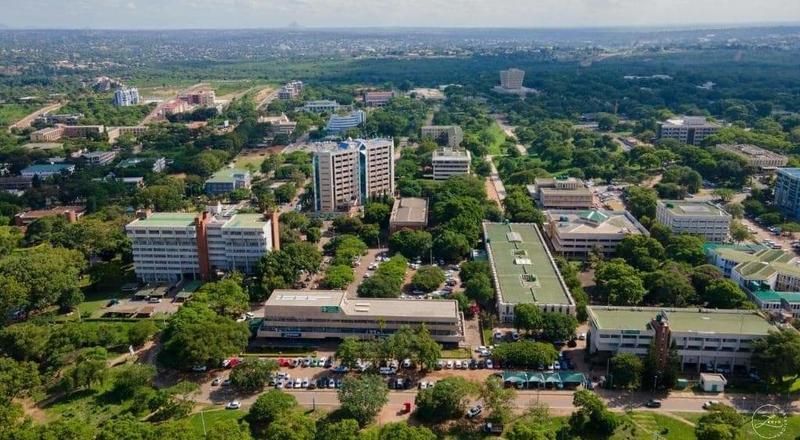 Una vista aerea di una città con edifici moderni che si ergono sopra fitti alberi verdi, con parcheggi e strade visibili sotto.