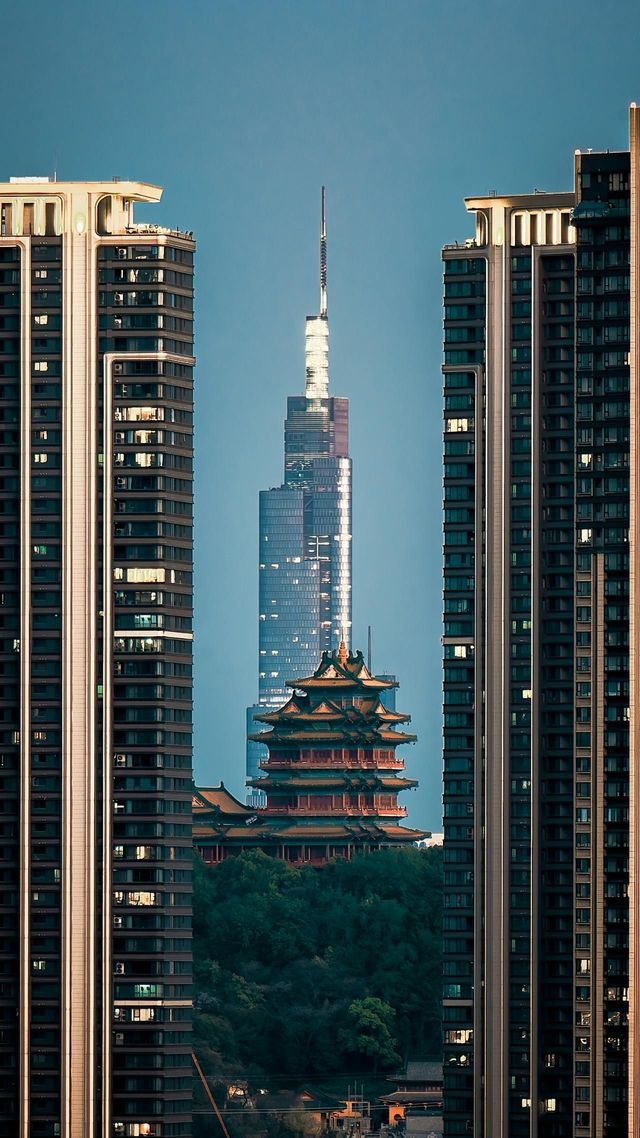 Una pagoda tradizionale su una collina e un moderno grattacielo sono incorniciati tra due alti condomini contro un cielo blu.
