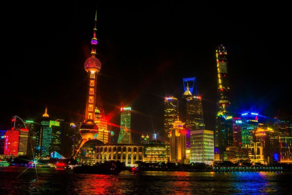 Uno skyline moderno della città, con una torre distintiva e grattacieli illuminati da luci colorate che si riflettono sull'acqua di notte.