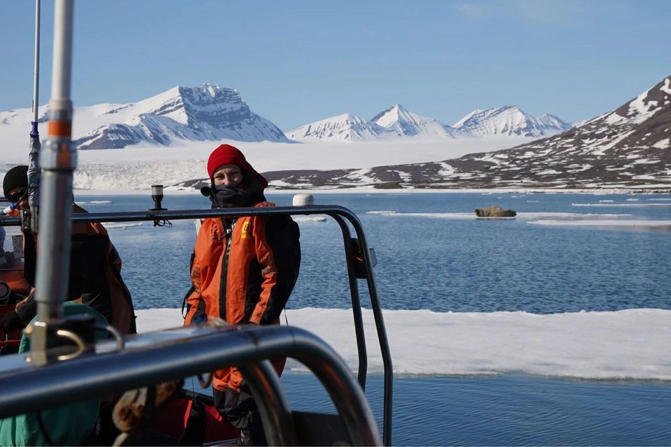 Una persona con chaqueta naranja y gorro rojo en un barco durante un viaje en grupo de WeRoad, con montañas nevadas y hielo en el agua.
