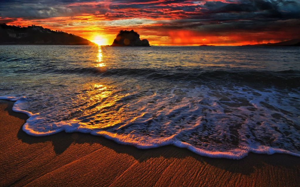 Un'onda delicata con schiuma bianca accarezza una spiaggia sabbiosa durante un tramonto colorato sull'oceano, riflettendosi sull'acqua.