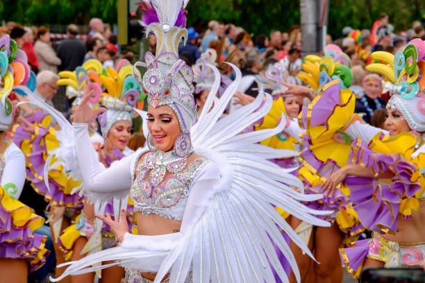 Una donna in un costume di carnevale bianco e ingioiellato con piume balla durante una sfilata di strada con altri artisti.