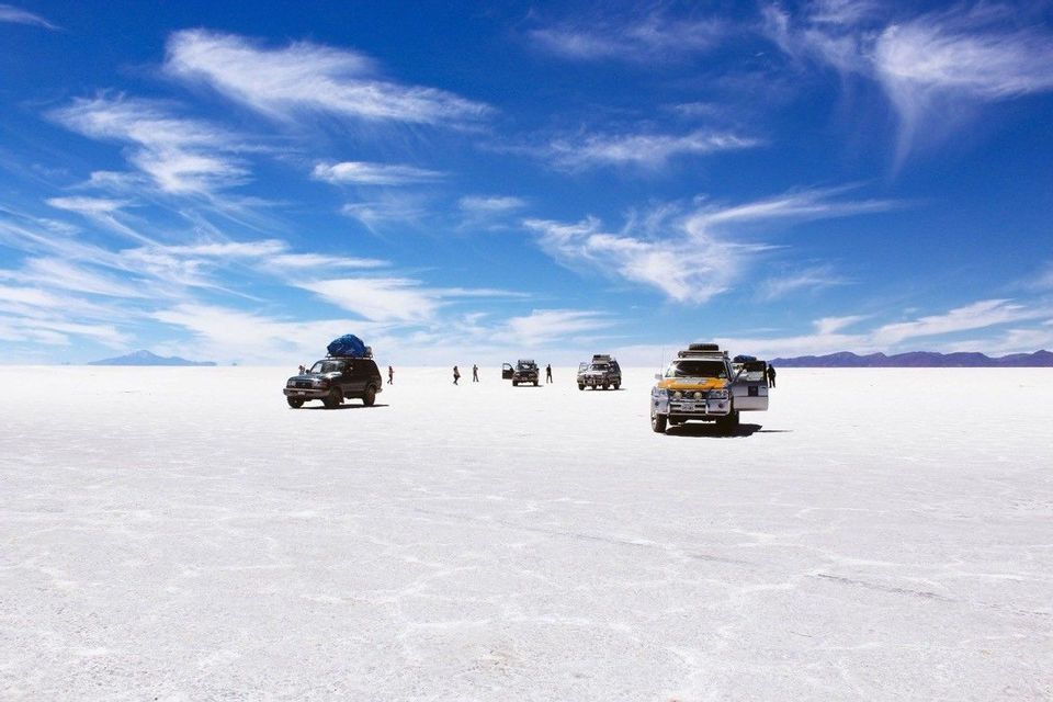 A WeRoad group trip with several off-road vehicles parked on a vast white salt flat under a bright blue sky.