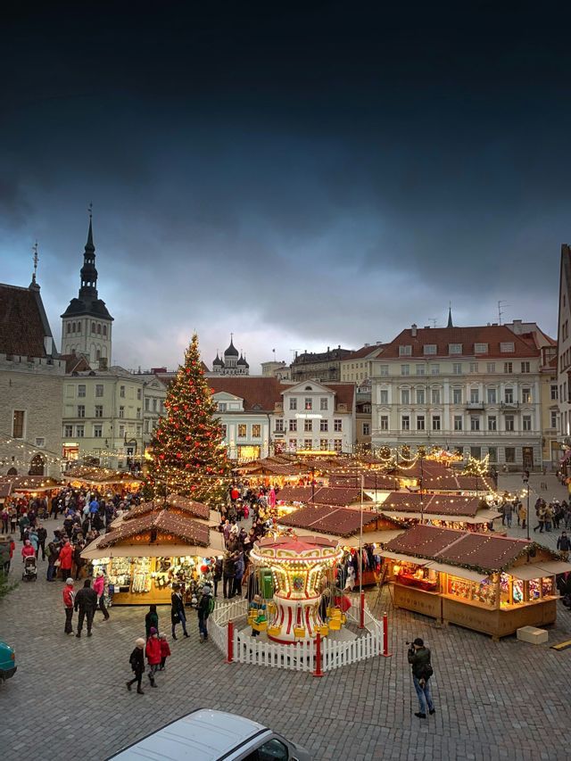 Un vivace mercatino di Natale in una piazza acciottolata con un grande albero di Natale illuminato, bancarelle e una giostra.