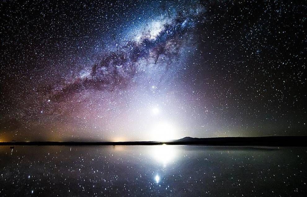 La Voie lactée et d'innombrables étoiles dans le ciel nocturne se reflètent parfaitement sur un plan d'eau calme à l'horizon.