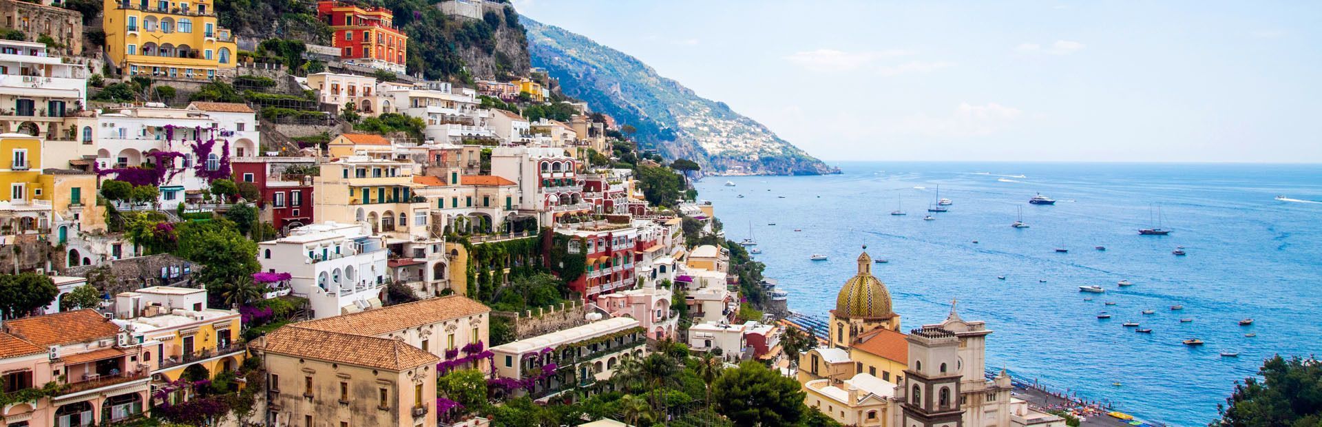 Una vista panoramica di una colorata città costiera costruita su una scogliera, che si affaccia su un mare blu con tante barche.