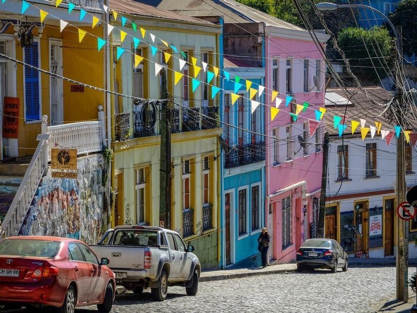Bandierine colorate pendono su una strada acciottolata fiancheggiata da vivaci edifici multicolori e auto parcheggiate.