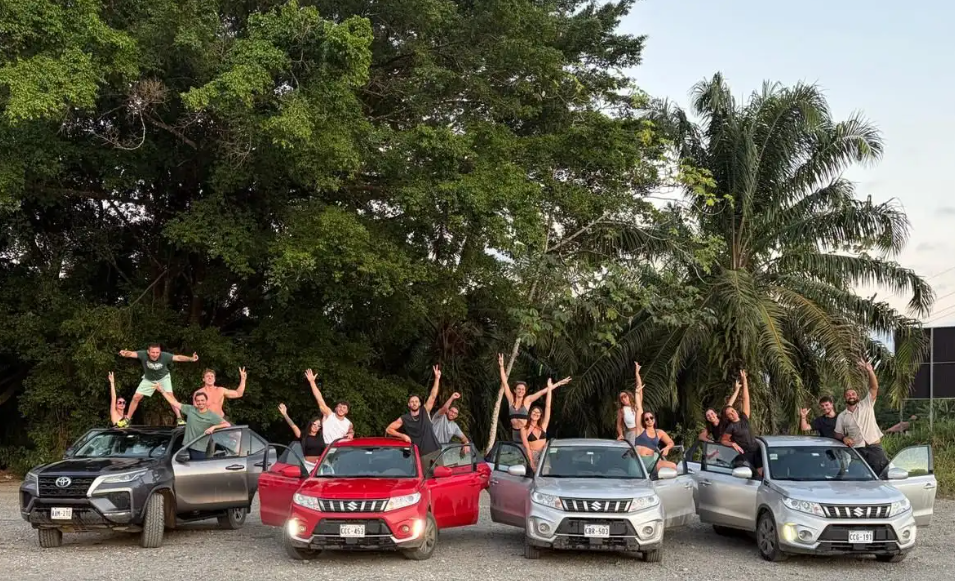 Un gruppo WeRoad in viaggio, con persone in posa su e intorno a quattro SUV parcheggiati davanti a rigogliosi alberi verdi.
