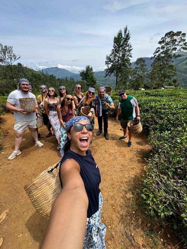 Un groupe WeRoad pose pour un selfie sur un sentier dans une plantation de thé, tenant des paniers tressés pour la cueillette du thé.