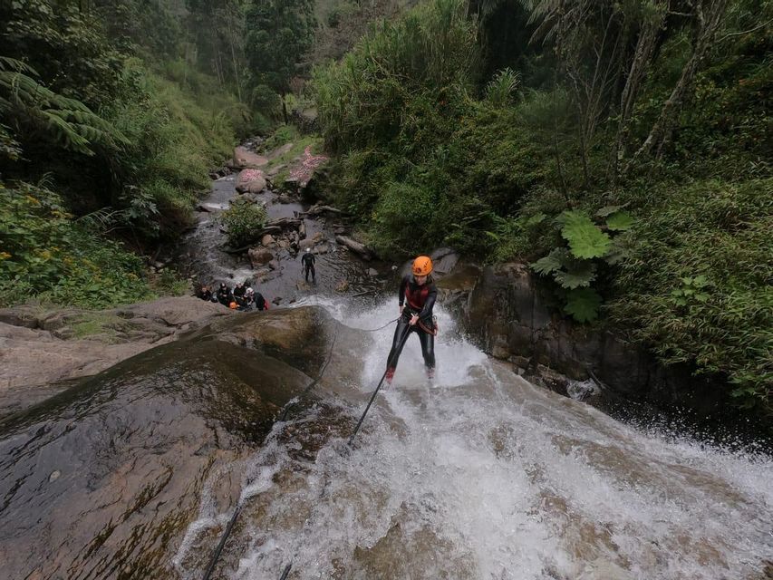 Una persona de un viaje en grupo de WeRoad haciendo rápel por una cascada caudalosa, con casco y traje de neopreno.