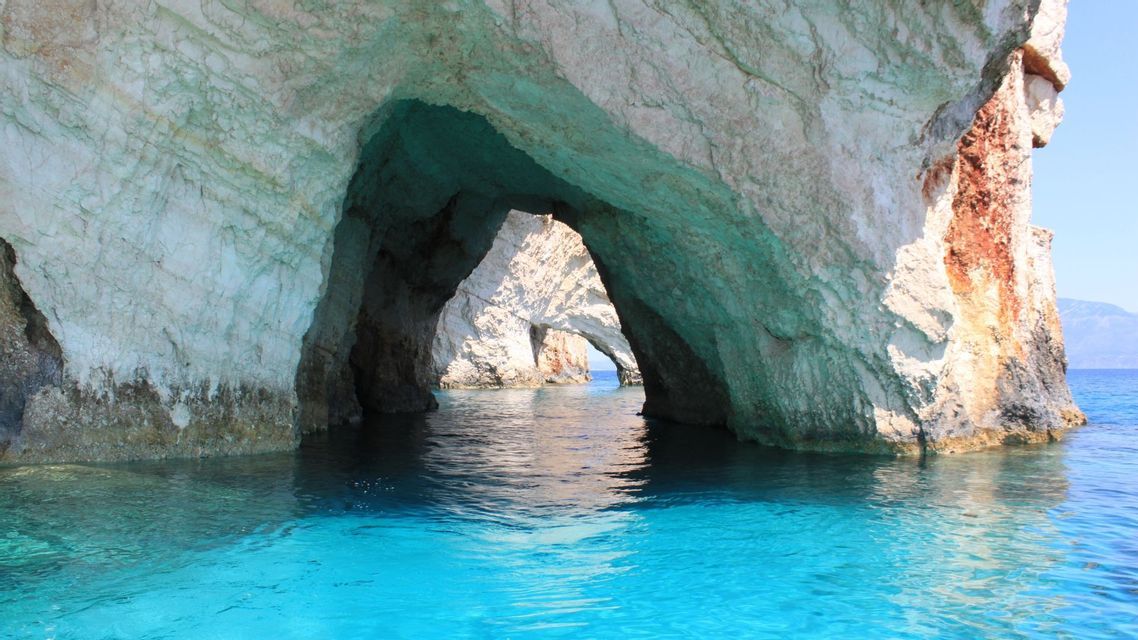 Una vista dall'acqua di grandi formazioni rocciose che creano archi naturali e grotte marine in acque turchesi brillanti.