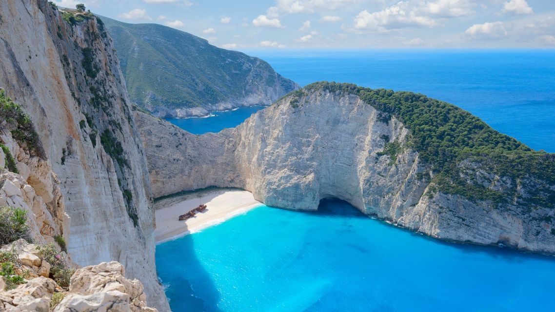 Un relitto arrugginito su una spiaggia isolata di sabbia bianca, circondata da alte scogliere bianche e acque turchesi.
