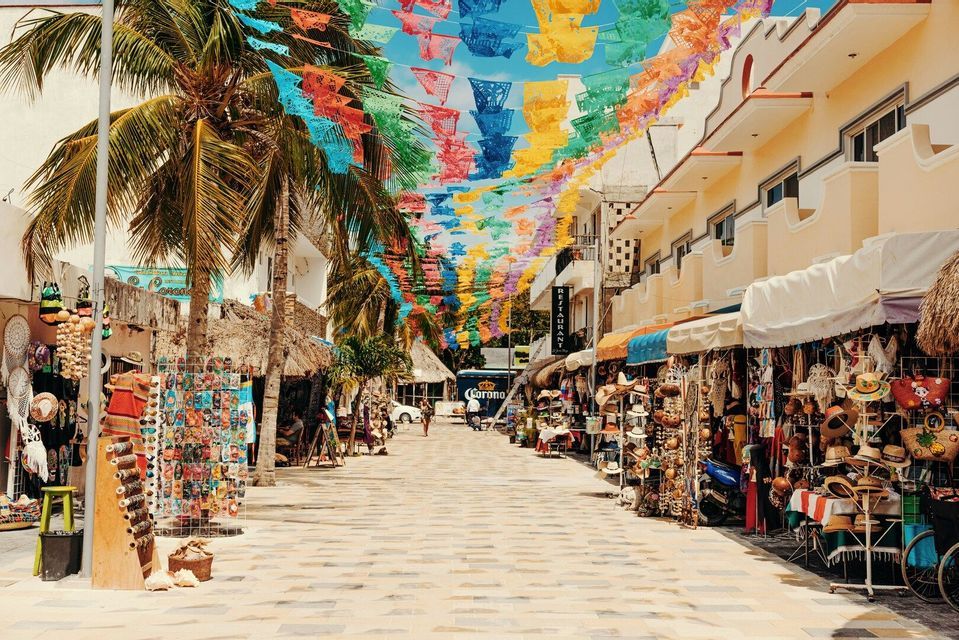 Striscioni decorativi colorati sono appesi lungo una strada pedonale soleggiata, fiancheggiata da palme e bancarelle di souvenir.