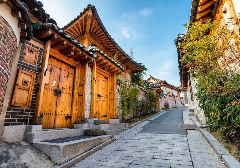 A narrow, paved street slopes uphill past traditional wooden houses with tiled roofs under a clear blue sky.
