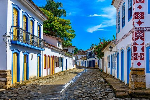 A wet cobblestone street lined with white colonial buildings featuring colorful blue and yellow doors and window frames.