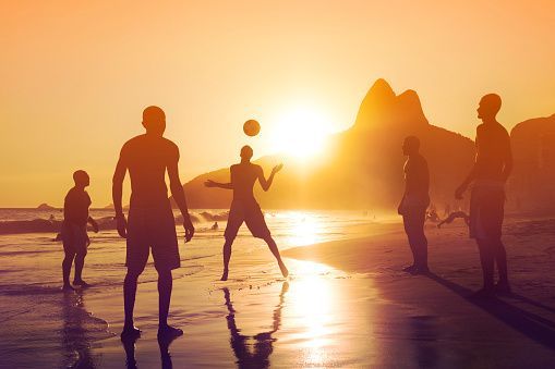 A WeRoad group trip playing with a ball on a beach, silhouetted against a golden sunset with mountains in the background.