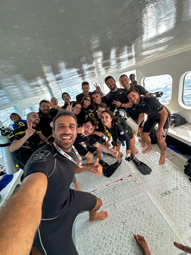 Eine WeRoad-Gruppenreise in Tauchausrüstung posiert für ein Gruppenselfie an Bord eines Bootes.
