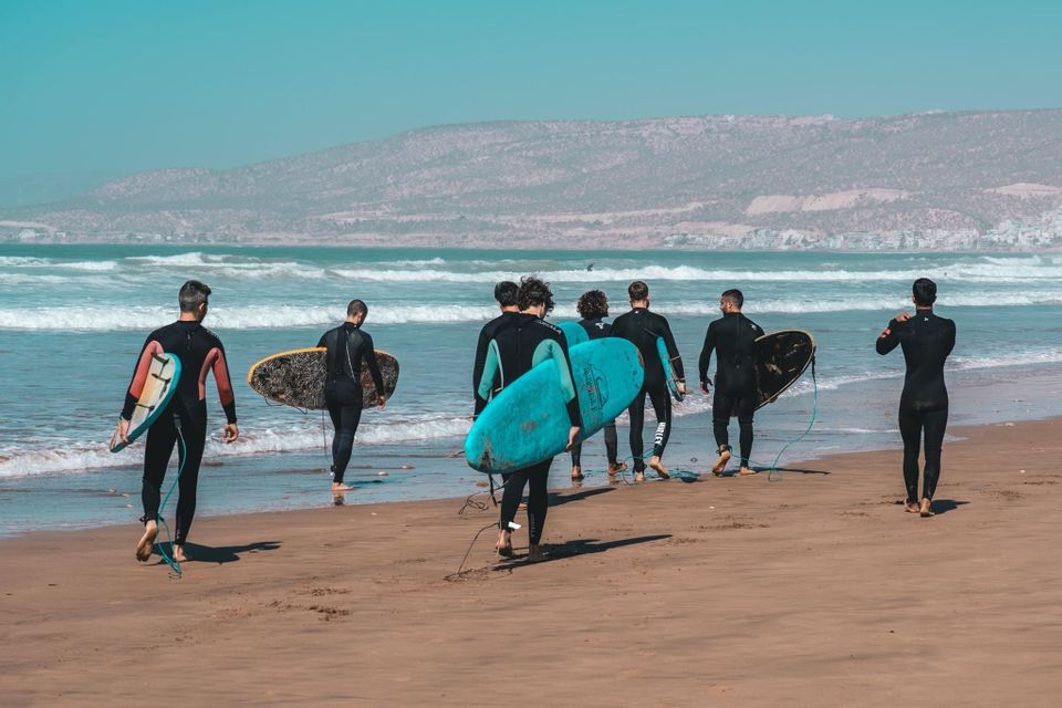 Un viaggio di gruppo WeRoad con persone in muta che trasportano tavole da surf e camminano verso l'oceano su una spiaggia sabbiosa.