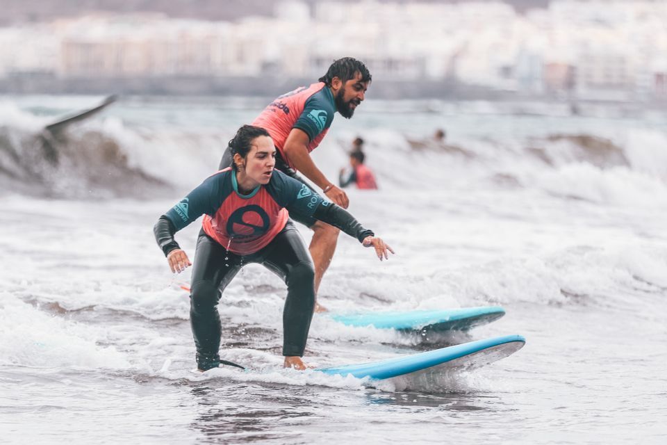 Una donna prende una lezione di surf da un istruttore in mare durante un viaggio di gruppo WeRoad.