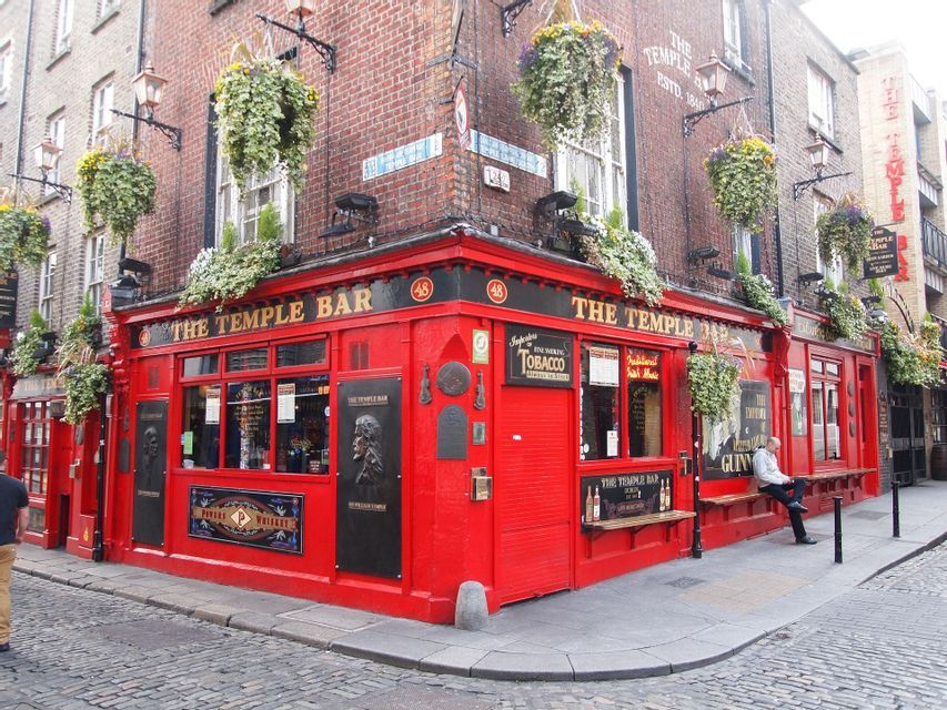 La facciata rosso brillante del pub The Temple Bar su un angolo di strada acciottolata, ornata da cesti di fiori appesi.