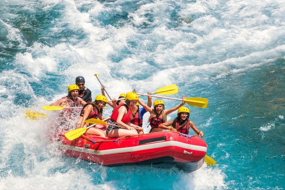 Eine WeRoad-Gruppe jubelt beim Wildwasser-Rafting in einem roten Schlauchboot auf unruhigem blauen Wasser.