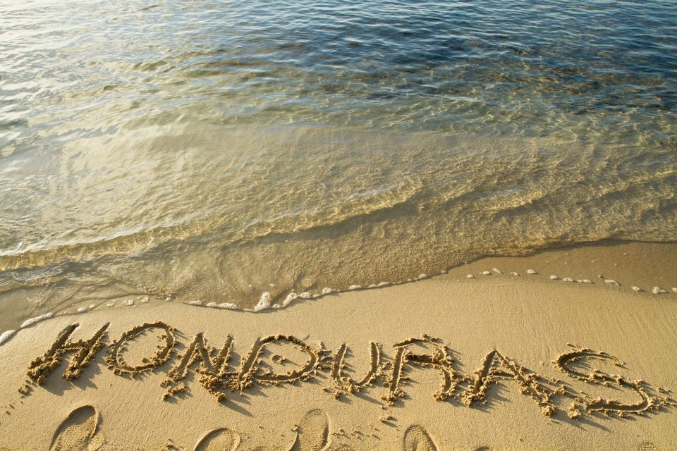 Das Wort Honduras ist in den Sand am Strand geschrieben, während sanftes Meerwasser ans Ufer gespült wird.