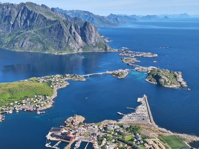 An aerial view of a coastal village built across several small islands connected by bridges, with a mountain range in the background.