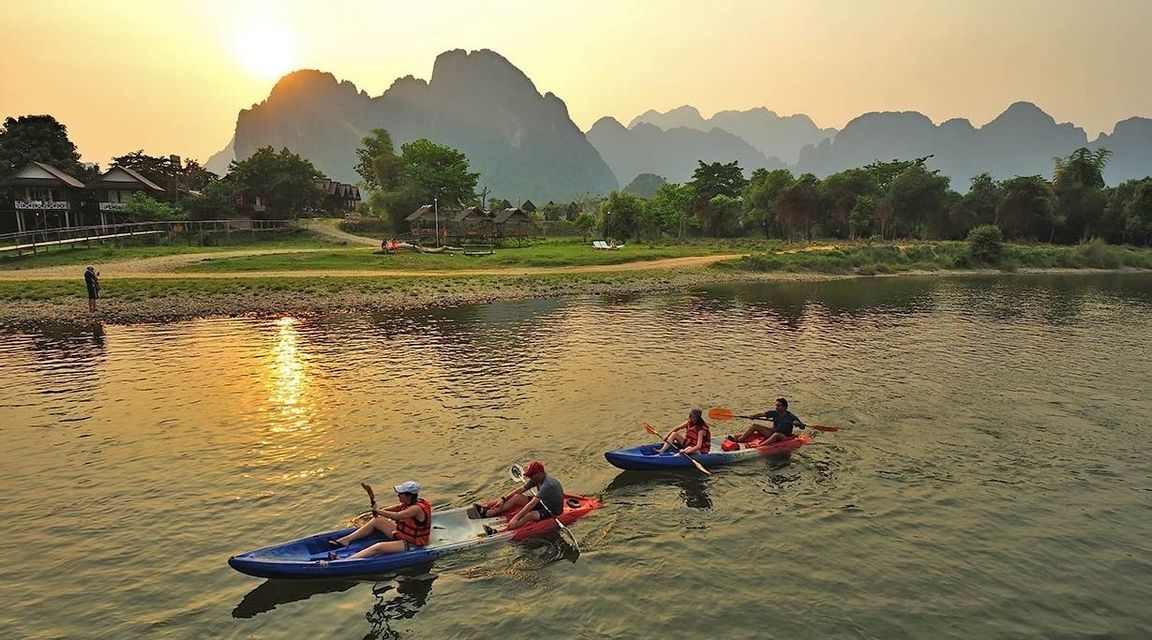 Un viaggio di gruppo WeRoad in kayak su un fiume tranquillo al tramonto, con grandi montagne stagliate sullo sfondo.