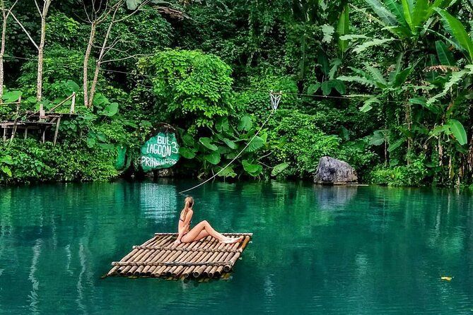 Una donna in bikini siede su una zattera di bambù che galleggia sulle acque calme e verdi di una laguna circondata da una giungla lussureggiante.