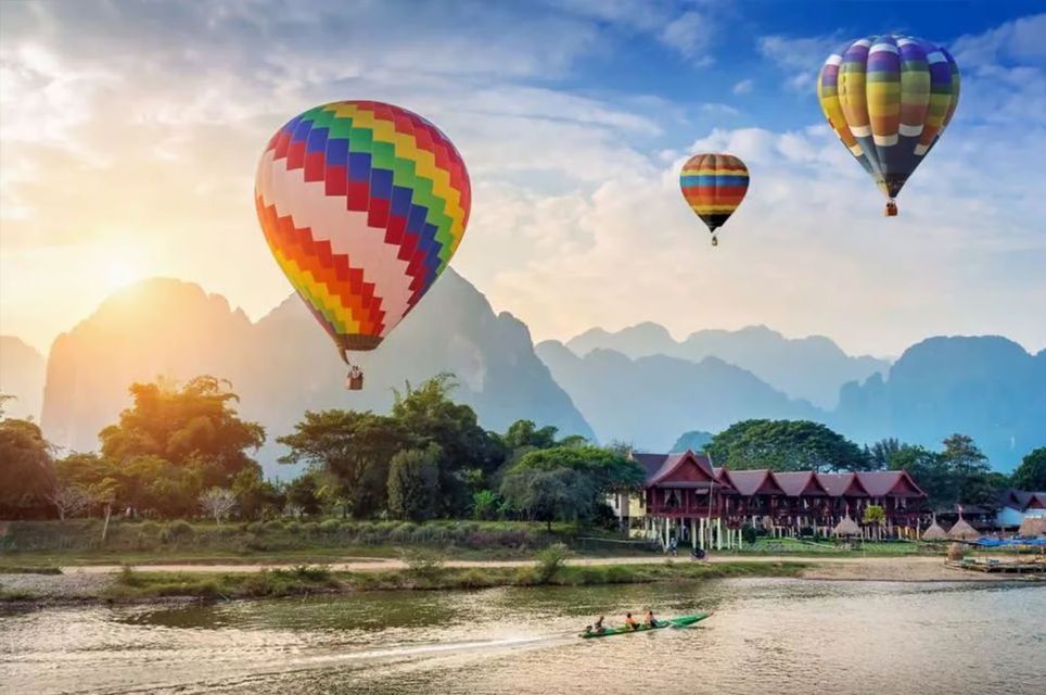 Mongolfiere colorate sorvolano un fiume con vegetazione rigogliosa e montagne durante un'alba scenografica.