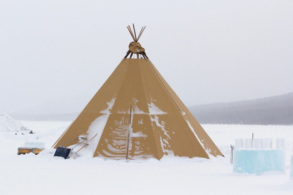 Un grande tipi color sabbia si erge in un paesaggio innevato, con una pala da neve e grandi blocchi di ghiaccio nelle vicinanze.