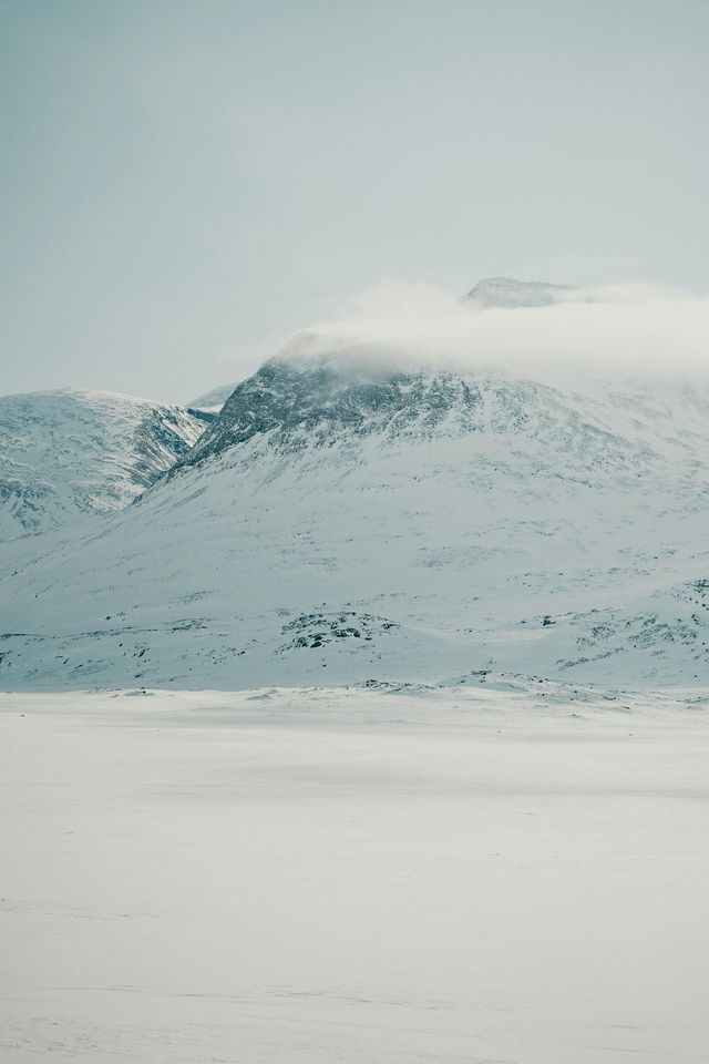 Una catena montuosa innevata con le sue cime avvolte dalle nuvole sotto un cielo pallido e coperto.