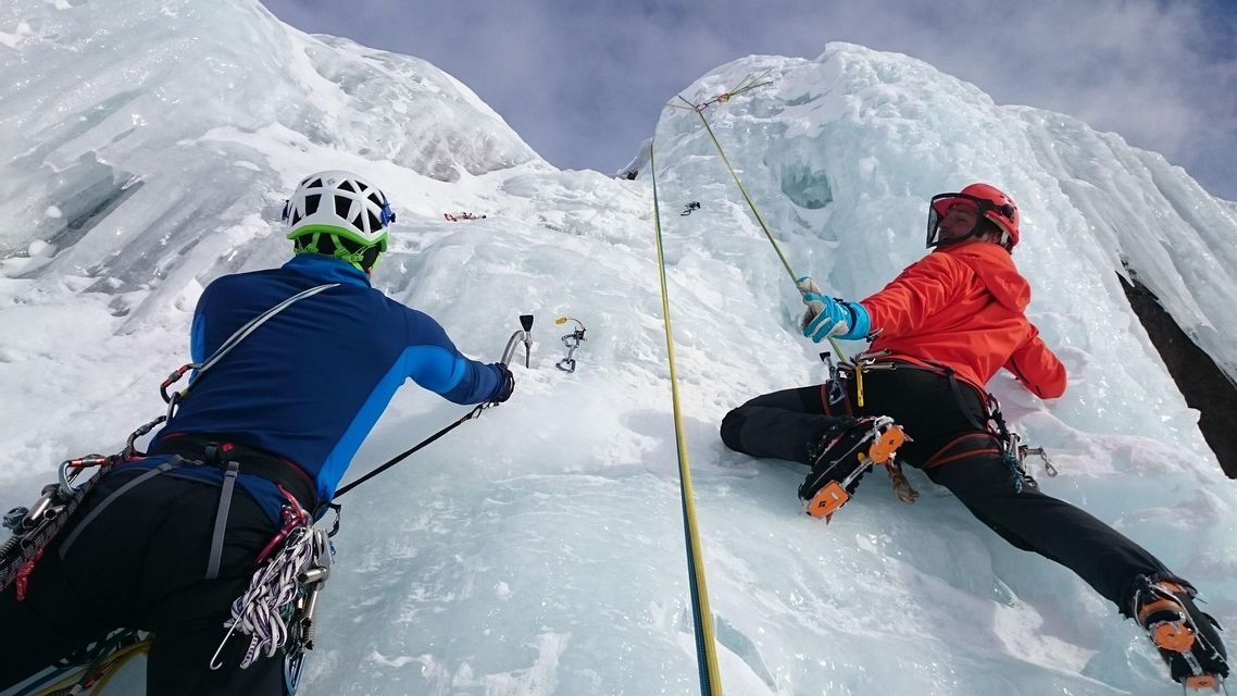 Due alpinisti di un gruppo WeRoad scalano una ripida parete di ghiaccio con corde e attrezzatura completa da arrampicata.