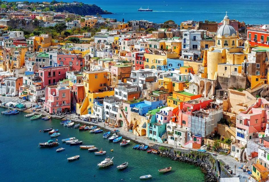 A high-angle view of a colorful coastal town with buildings packed onto a cliffside overlooking a harbor full of boats.