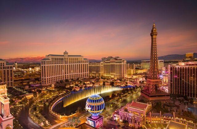 Un horizonte urbano iluminado con una réplica de la Torre Eiffel, edificios de hoteles y fuentes al atardecer