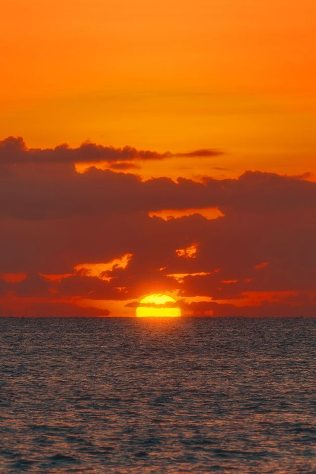 Le soleil jaune se couche sur l'horizon de l'océan sous un ciel orange vif rempli de nuages sombres.