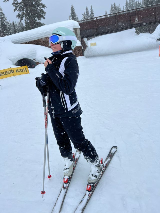 Una persona con casco y gafas de ventisca está de pie sobre unos esquís en una pendiente nevada mientras sostiene bastones de esquí.