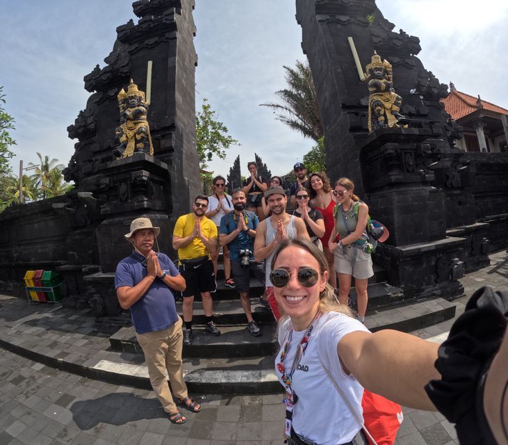 Un viaje en grupo de WeRoad posa para una selfie con un guía, haciendo un gesto de oración frente a una tradicional puerta de piedra negra.