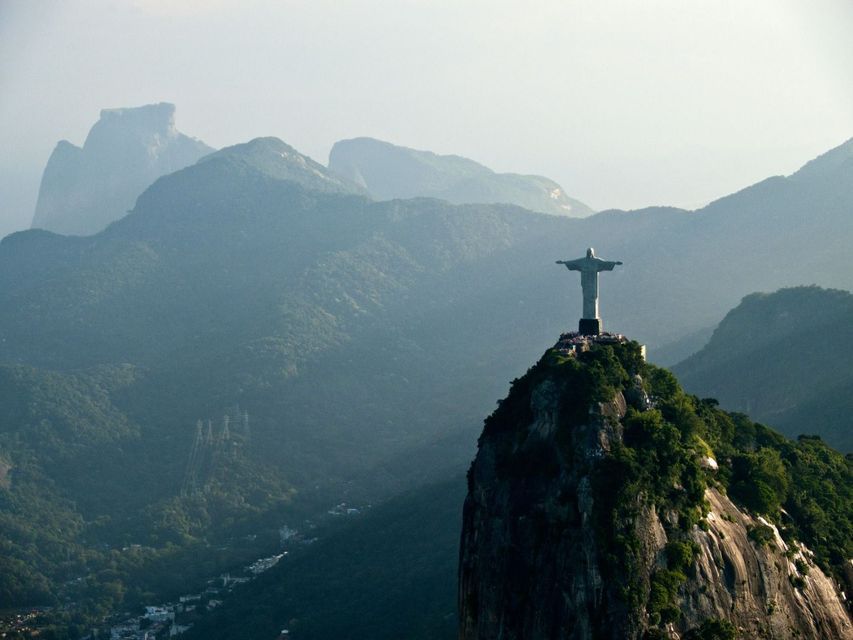 La statua del Cristo Redentore si erge su una cima di montagna, dominando un vasto paesaggio di montagne verdi e sfumate.