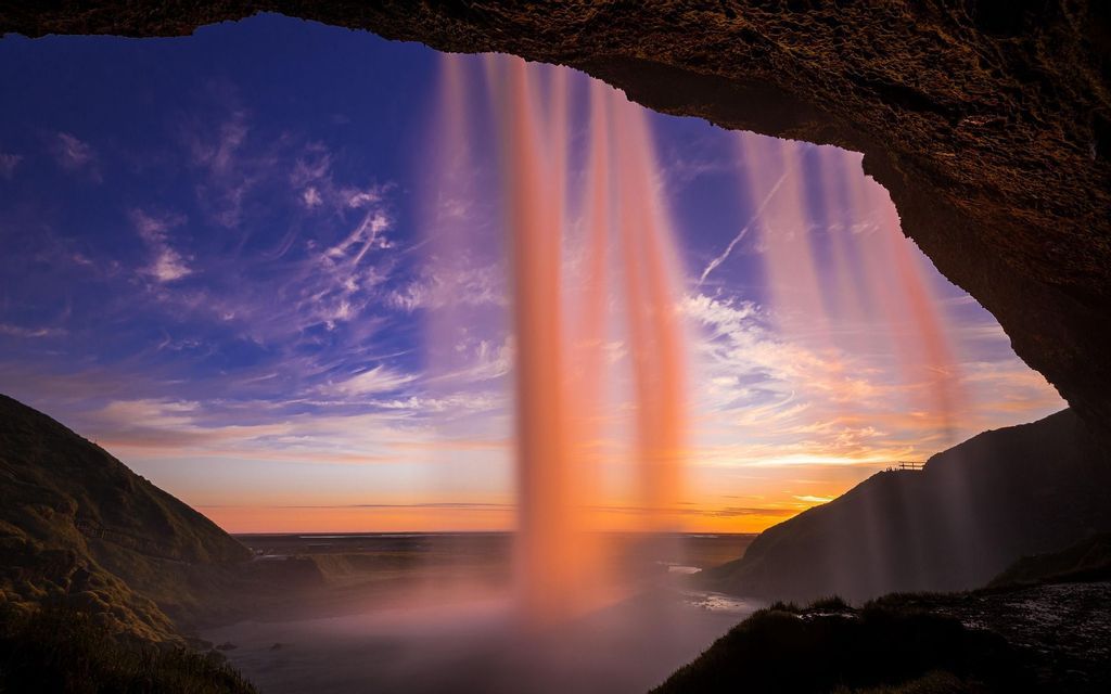 Una vista a lunga esposizione da dietro una cascata, illuminata da un tramonto colorato su una valle.